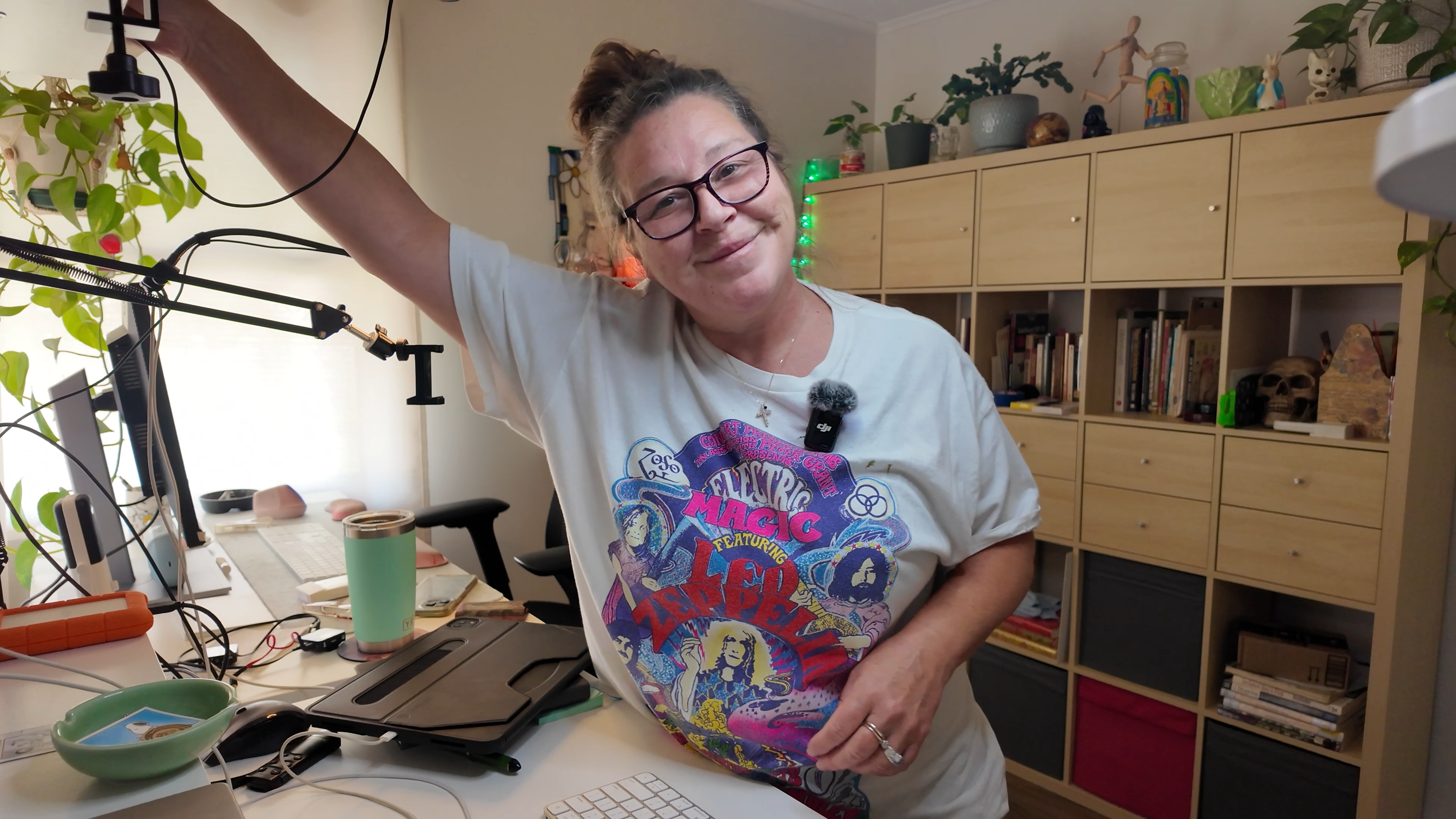 The Artist Penelope Wrenn, in a colorful t-shirt, standing in her art studio smiling at camera. Content creating brings joy to her face.